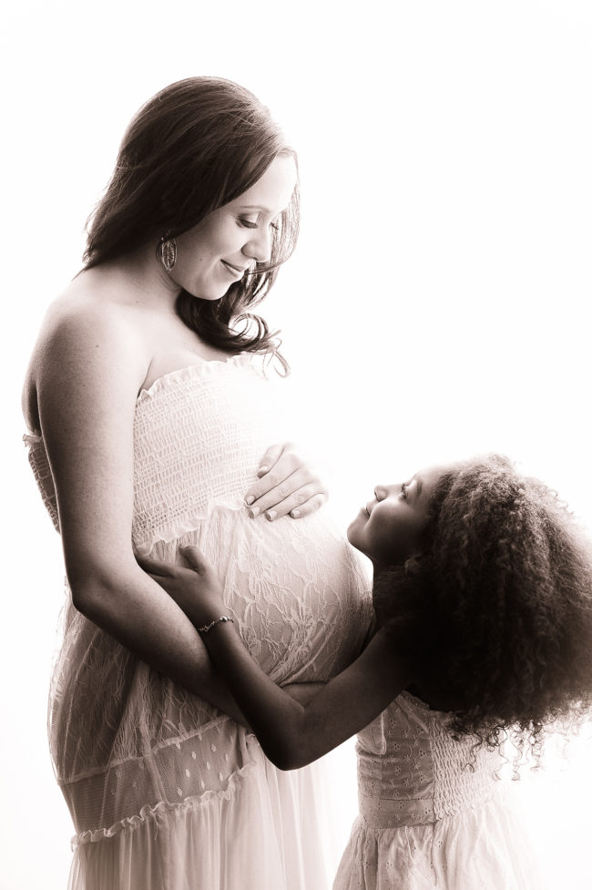 Pregnant mother and daughter holding belly